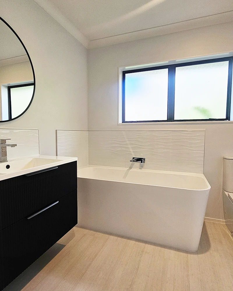 A modern bathroom renovation with a white bath, white walls, and a bathroom vanity in the corner.