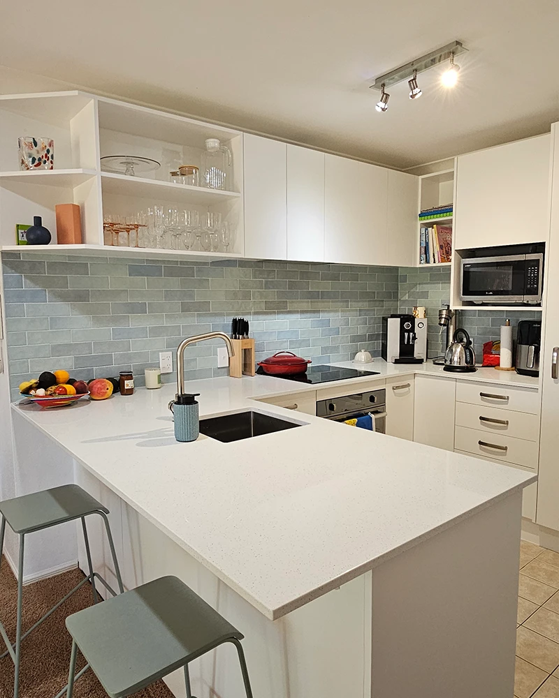 Kitchen with white stone countertop installed by Home Improvement Specialist. The kitchen has plates on it with bar stools along the counter.
